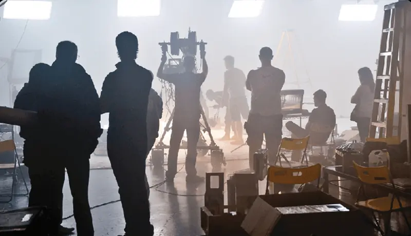 A camera operator filming a person speaking on a set
