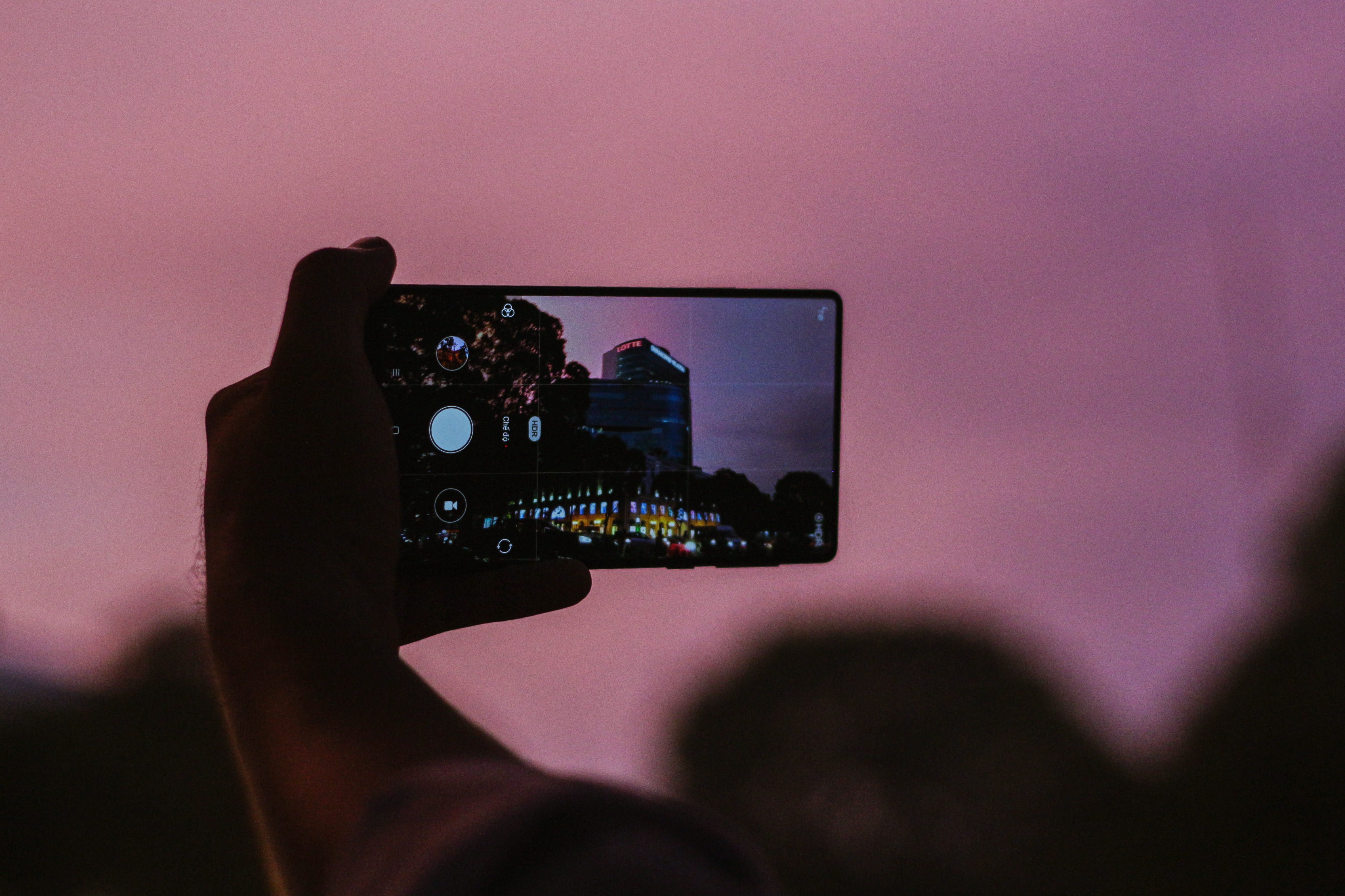 Large phone taking photo of a building with pink sky